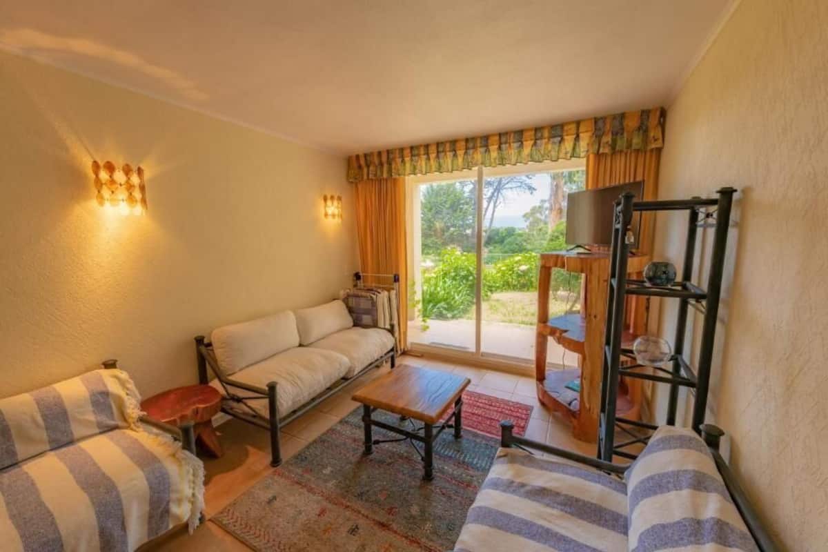 Une pièce confortable avec un canapé, une petite table, un téléviseur et une étagère ornée d’objets décoratifs.