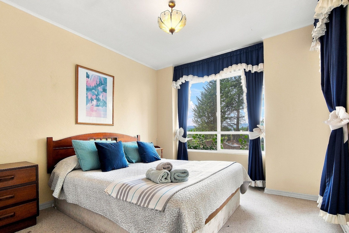 Une chambre à coucher avec un lit, une table de chevet, une fenêtre avec des rideaux et un tableau au mur.
