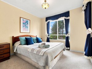 Une chambre à coucher avec un lit, une table de chevet, une fenêtre avec des rideaux et un tableau au mur.