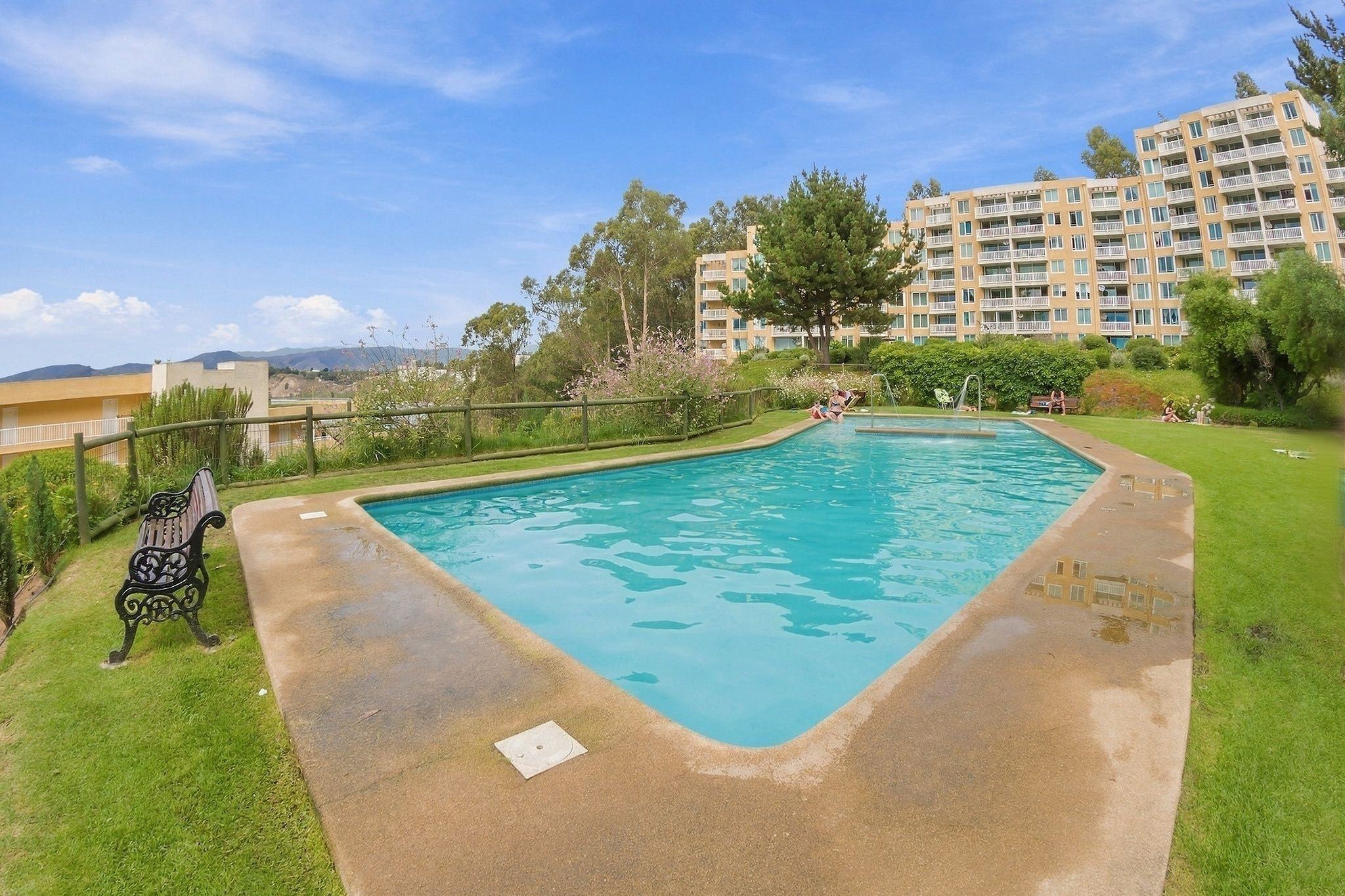 A rectangular swimming pool with a concrete edge, surrounded by a grassy area and a wooden fence.