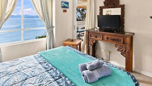 A bedroom with a bed, a television, and a view of the sea.