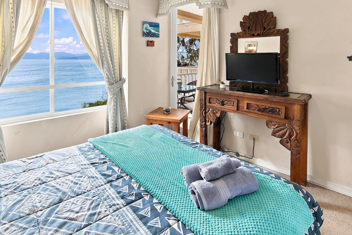Een slaapkamer met een bed, een televisie en uitzicht op zee.
