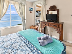 Een slaapkamer met een bed, een televisie en uitzicht op zee.
