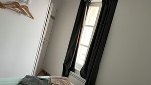 Une chambre à coucher avec un lit, une fenêtre avec des rideaux, un radiateur et un porte-manteau mural.
