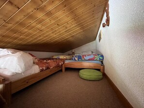 Une petite pièce fermée, avec deux lits superposés en bois, un coussin vert et un mur blanc.