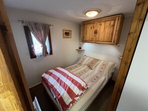 Een slaapkamer met een bed, een raam met gordijnen, een houten kast en een wandplank.
