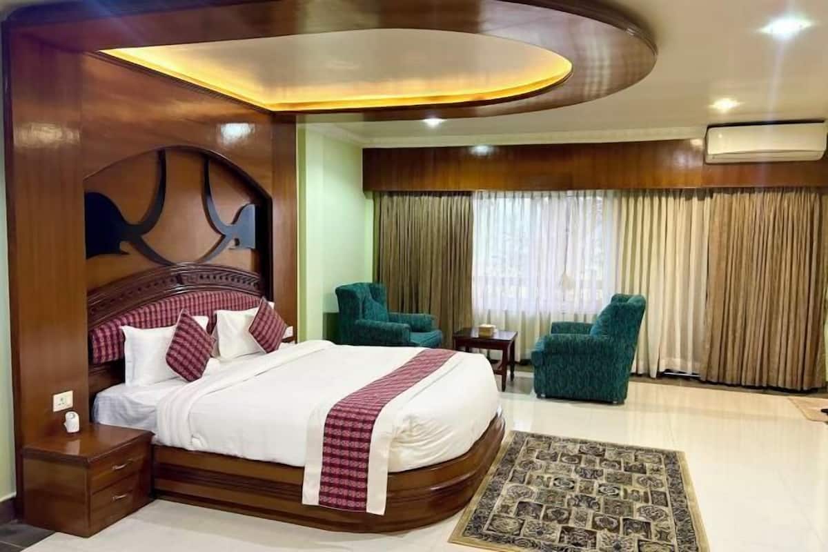 Habitación de hotel con una cama grande, dos sillones, una mesita y un cabecero decorativo.