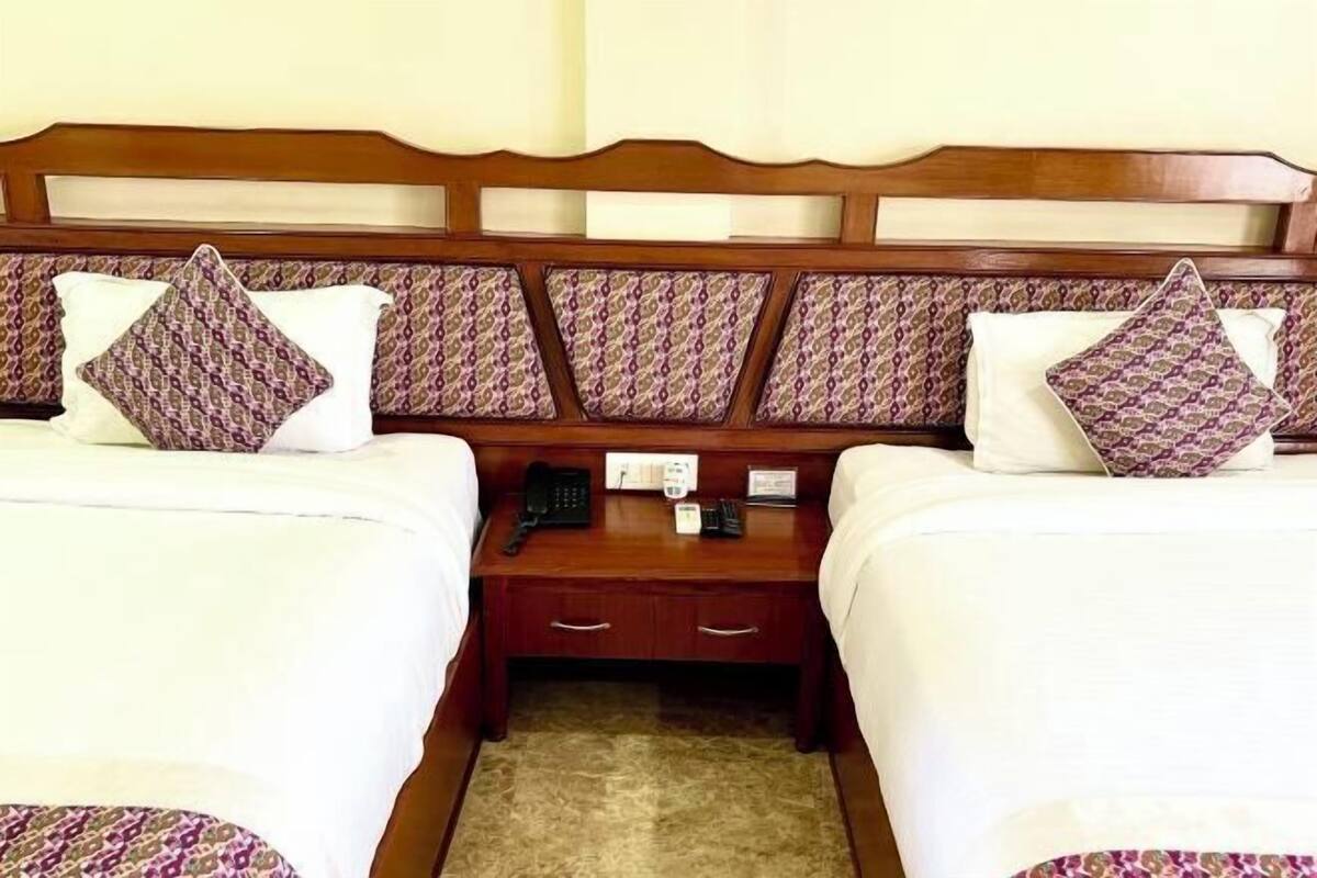 Habitación de hotel con dos camas, cabecero de madera, mesita de noche con teléfono y un cajón pequeño.