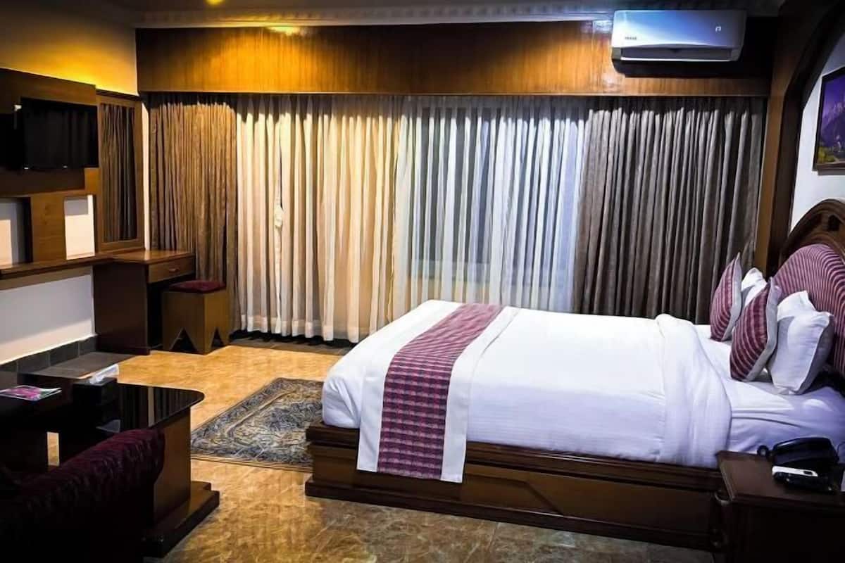 Habitación de hotel con cama, escritorio, silla, televisor y ventana con cortinas.