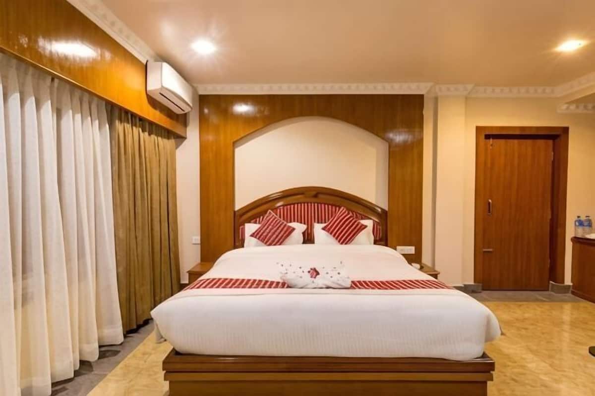 Una habitación de hotel con una cama grande, cabecero de madera, cortinas blancas, un armario de madera y una puerta.