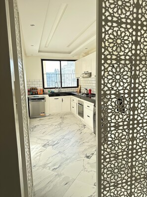 Una cucina moderna con mobili bianchi, un'ampia finestra e un pavimento in marmo.