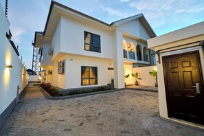 A modern two-story house with a paved driveway, a dark front door, and a balcony with plants.