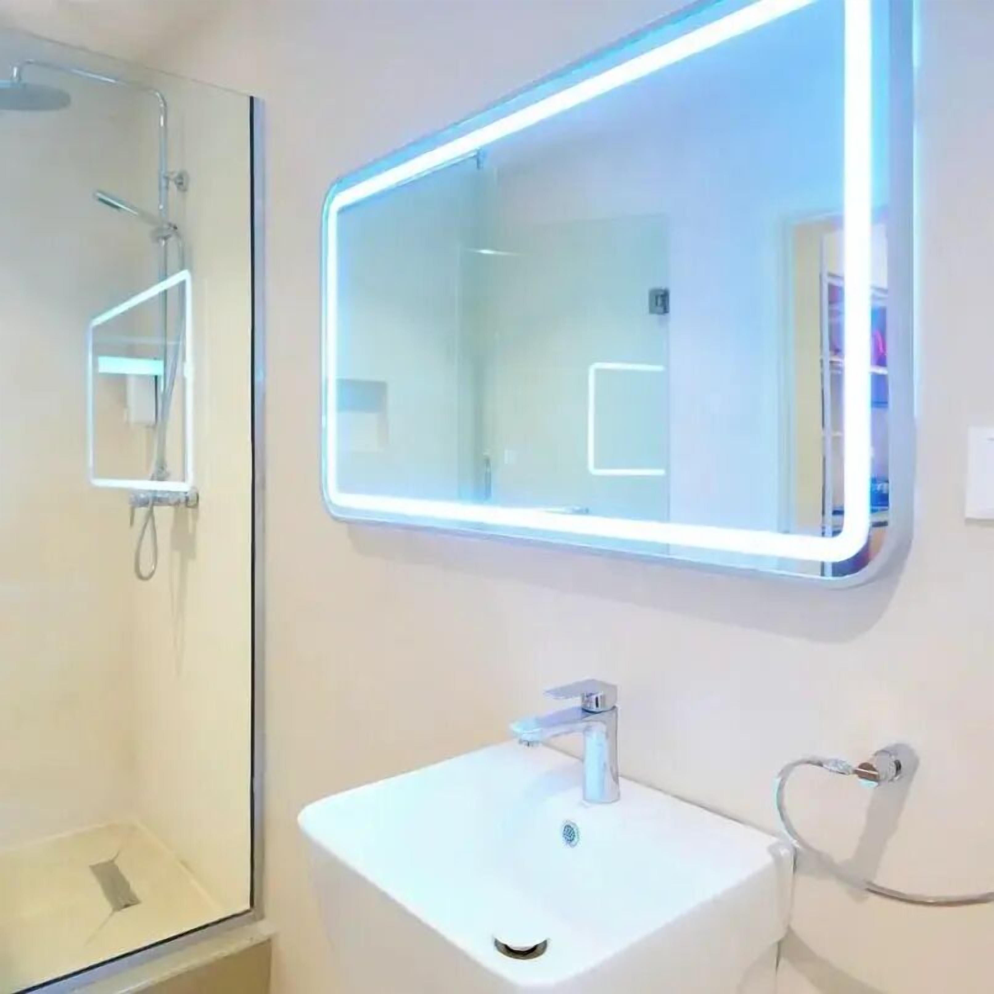 A modern bathroom with a white sink, a mirror with LED lighting, and a shower.