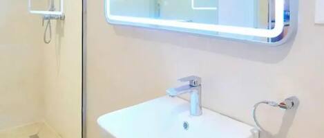 A modern bathroom with a white sink, a mirror with LED lighting, and a shower.