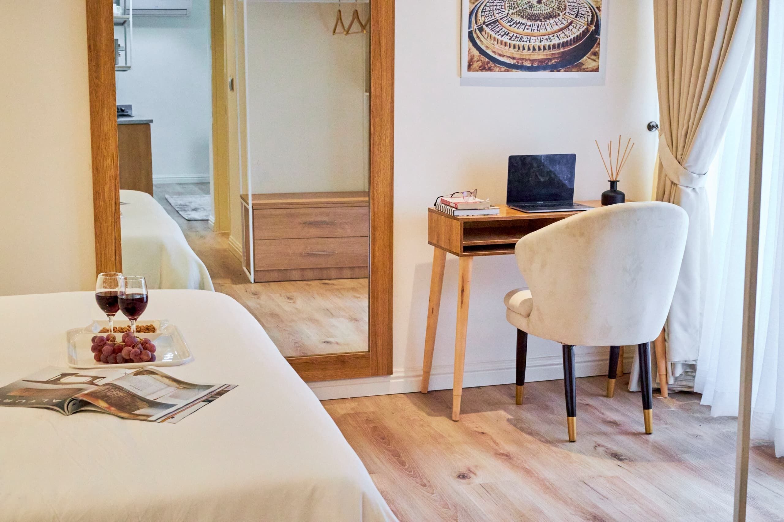 Een hotelkamer met een bed, een bureau met een laptop, een stoel en een eettafel met wijnglazen en druiven.