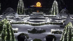 A snow-covered garden with illuminated pathways and trees, featuring a central circular area with a glowing sphere.