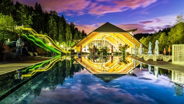 A hotel with a pool reflecting the surrounding trees and a green slide.