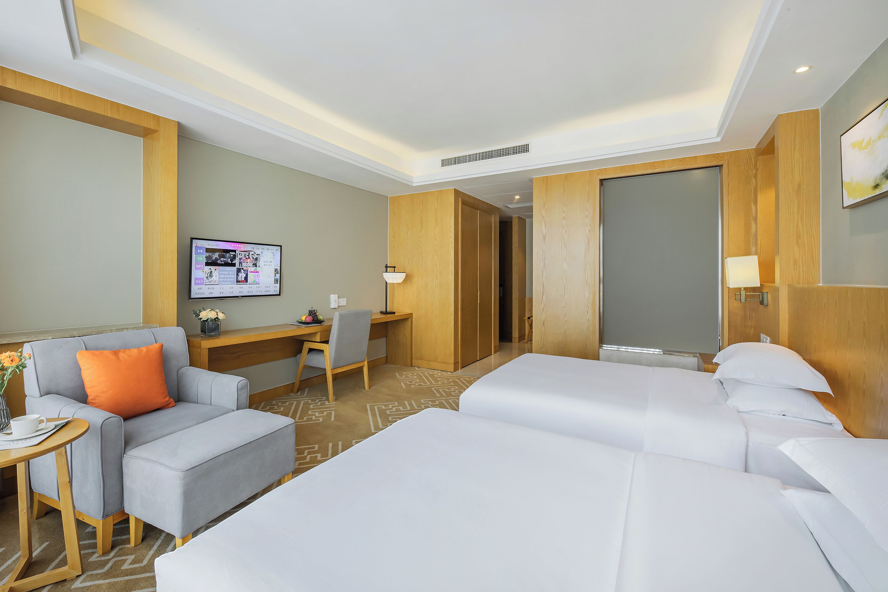 A hotel room with two beds, a desk, a chair, and a small sofa.