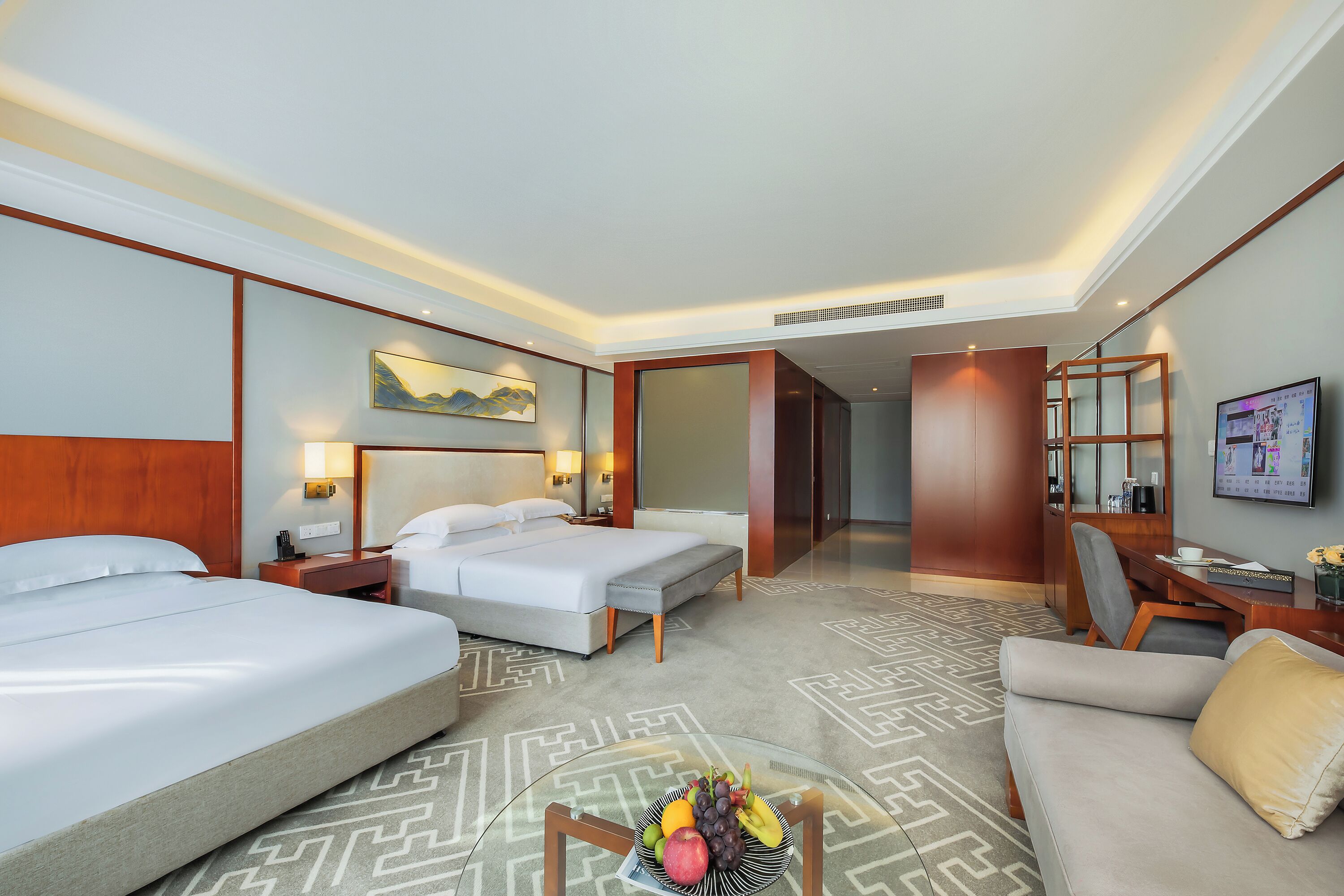 A hotel room with two beds, a sofa, a dining table, and a TV.