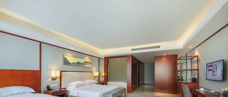 A hotel room with two beds, a sofa, a dining table, and a TV.