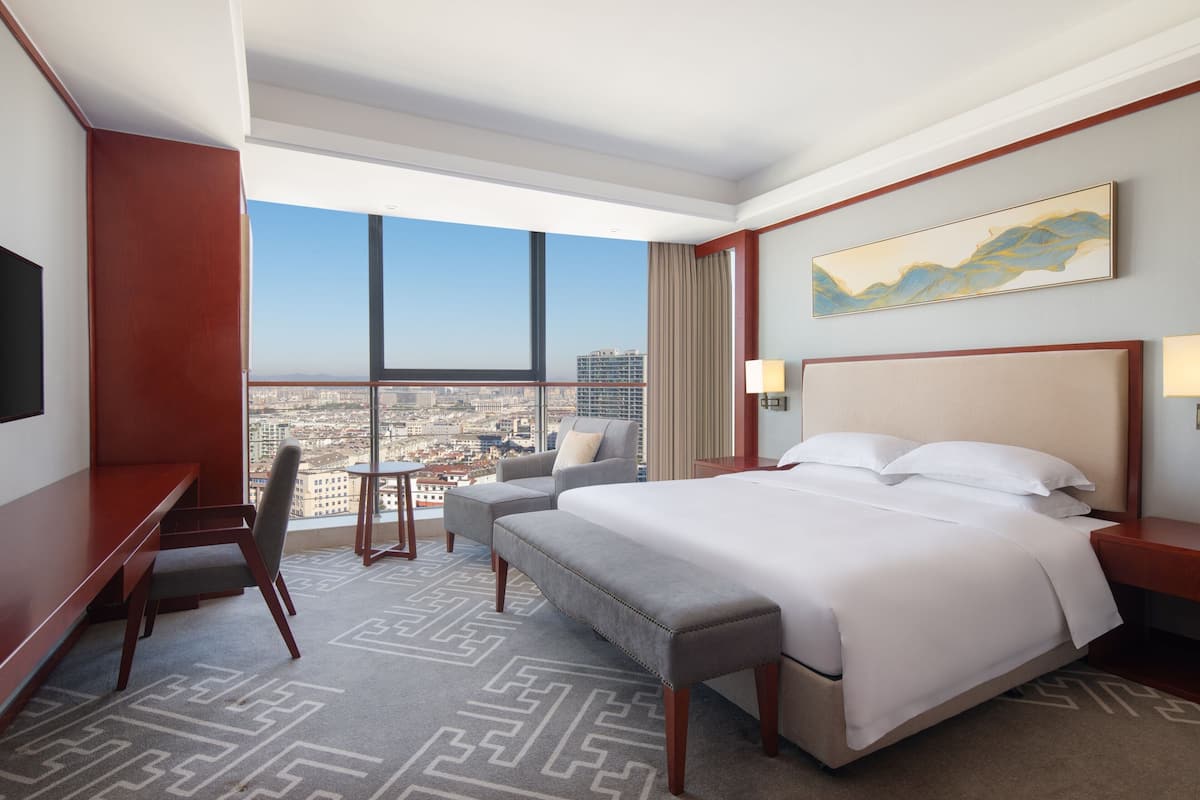 A hotel room with a large bed, a desk, a chair, and a view of the city.