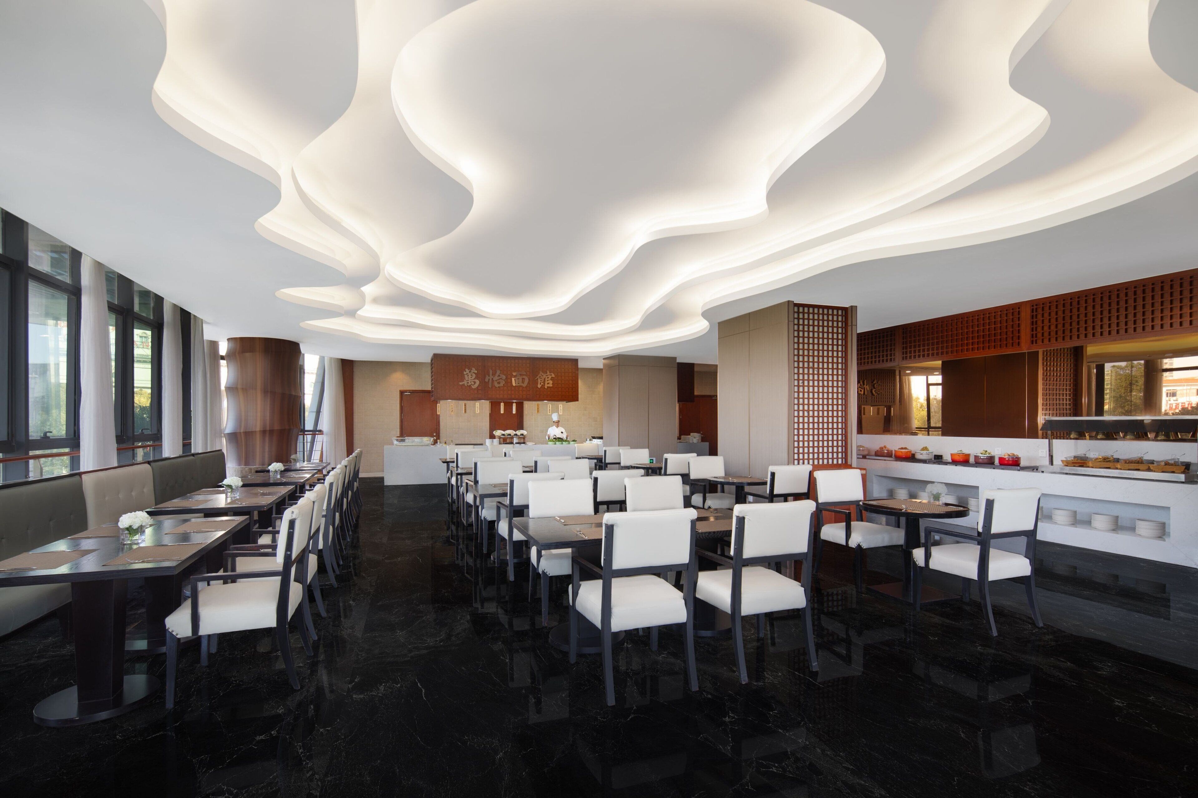 A modern restaurant with a long dining area, a bar, and a kitchen visible through an open layout.