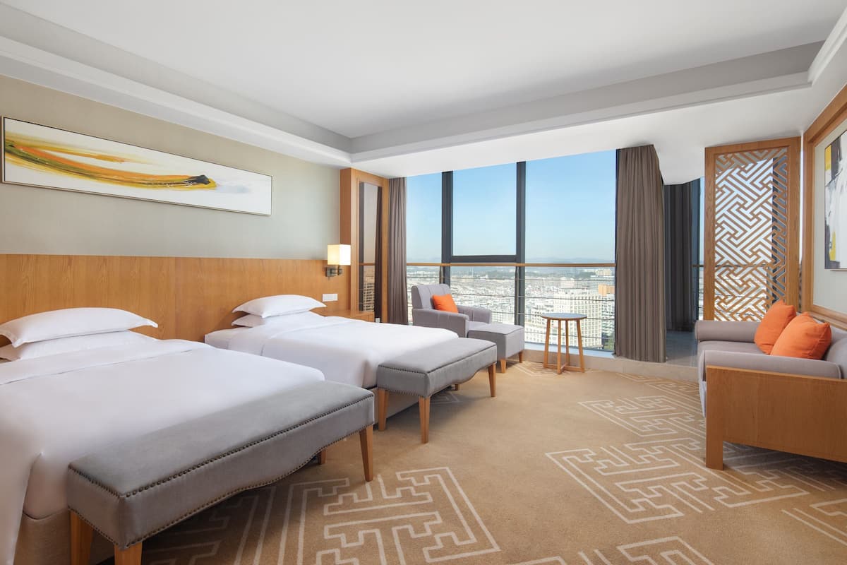A hotel room with two beds, a sofa, a chair, and a view of the city.