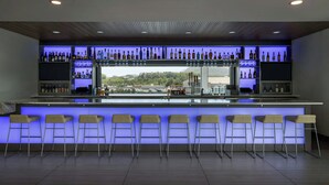 A bar area with a long counter, multiple stools, and shelves stocked with bottles. - Element by Marriott Cartersville (Cartersville)