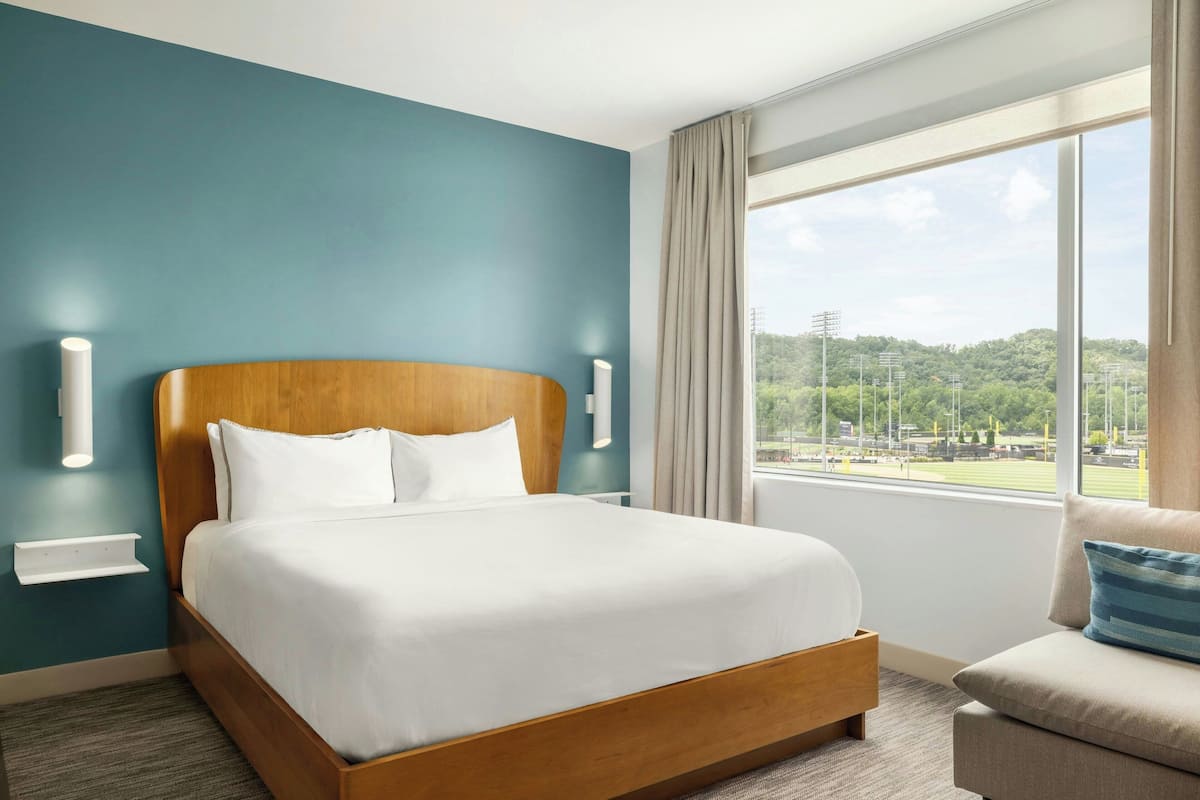 Ett modernt hotellrum med en stor säng, utsikt över en sportplan och en sittgrupp med utsikt.