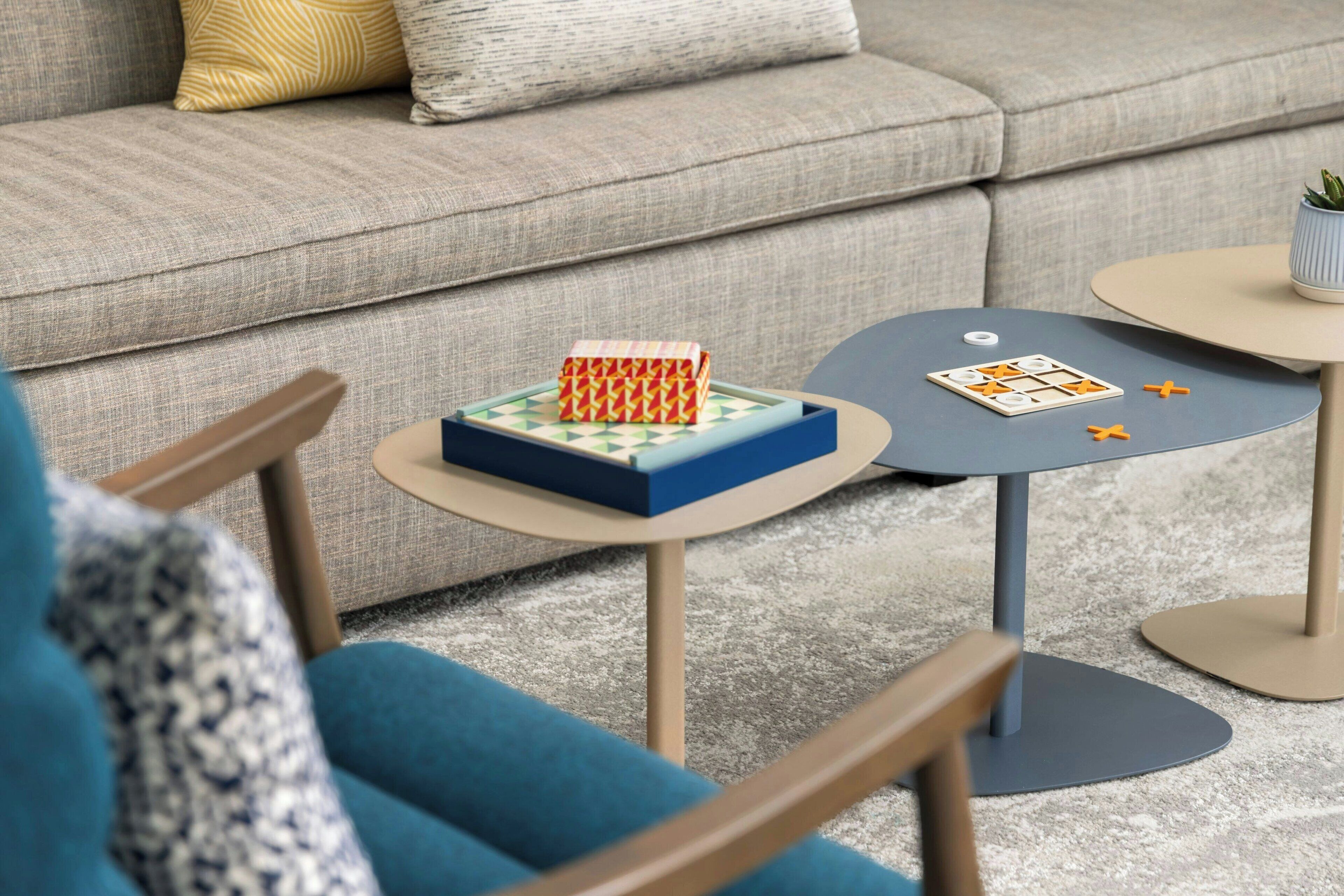 A living room with a grey sofa, a small round table with a board game, and a blue chair.