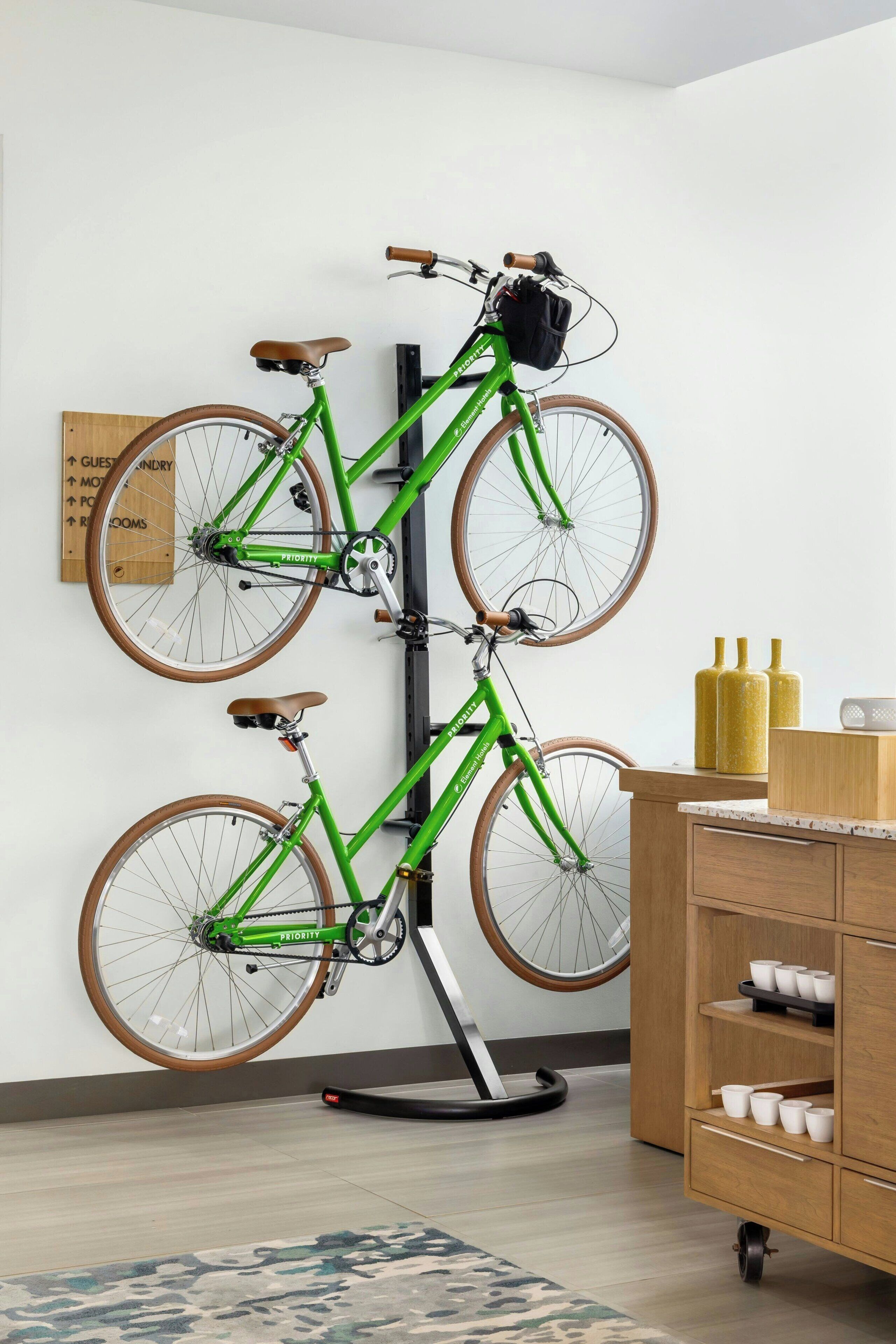 A room with a green bicycle mounted on a wall, a wooden cabinet with cups, and a sign with room directions.