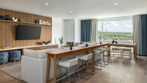 A modern living room with a wooden TV stand, a sofa, and a dining area with bar stools. - Element by Marriott Cartersville (Cartersville)