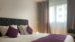 Un lit bien fait, avec une tête de lit sombre, des oreillers blancs et violets, et un plaid violet.