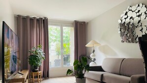 Un salon moderne avec un canapé, une table basse, un téléviseur et deux plantes en pot.