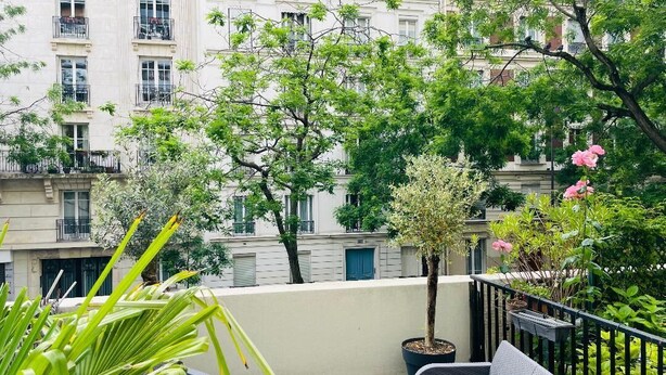 Un balcon avec un canapé, des plantes en pot et une vue sur un immeuble doté de nombreuses fenêtres et de balcons.