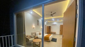A hotel room with a balcony, a bed, a sofa, a small table, and a ceiling fan. - Creek Wood (Ramnagar)