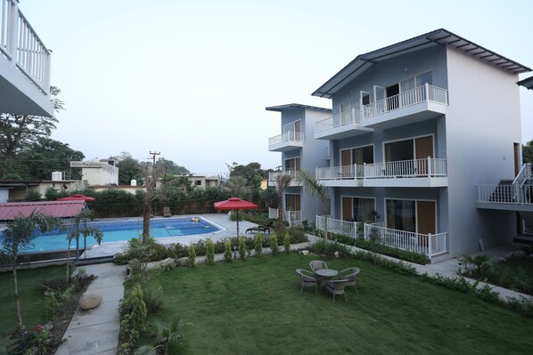 A modern hotel with a swimming pool, outdoor seating, and a well-maintained garden.