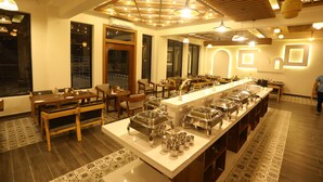 A spacious dining area with a long counter, multiple seating arrangements, and a variety of lighting fixtures. - Creek Wood (Ramnagar)