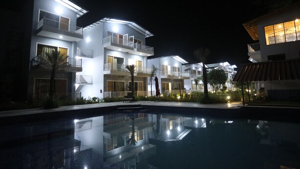 A modern hotel with multiple balconies, a swimming pool, and well-lit outdoor areas. - Creek Wood (Ramnagar)