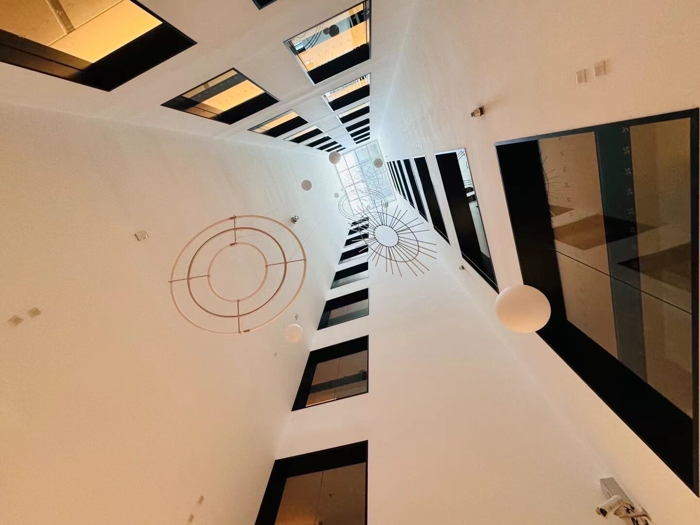 A modern interior with a central circular design on the ceiling, multiple windows, and a glass partition on the right.
