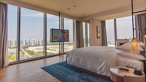 A modern hotel room with a large bed, a TV mounted on the wall, and a city view through large windows. - Four Points By Sheraton Yantai (Yantai)