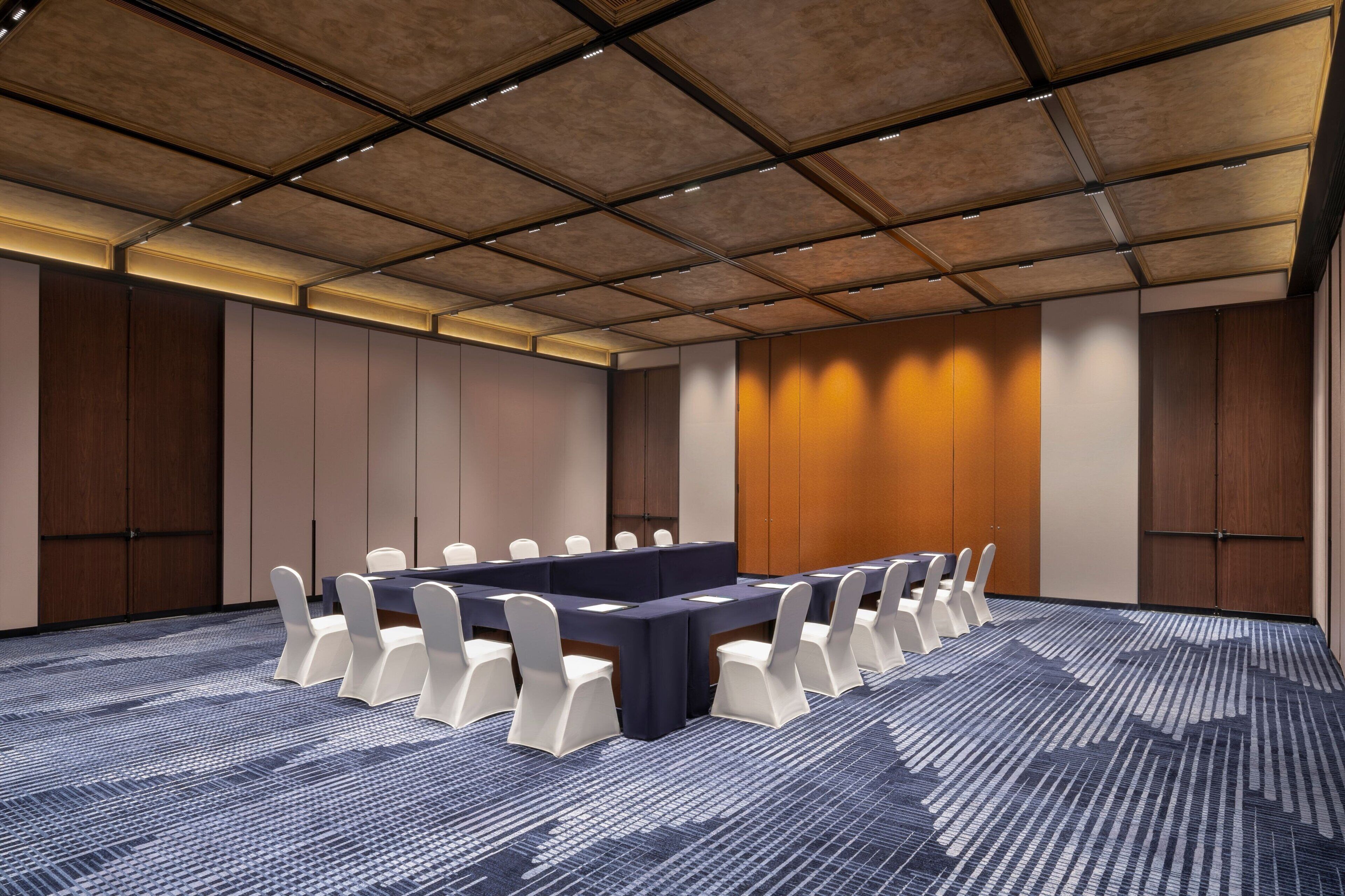 A conference room with a long table, white chairs, and a patterned carpet.
