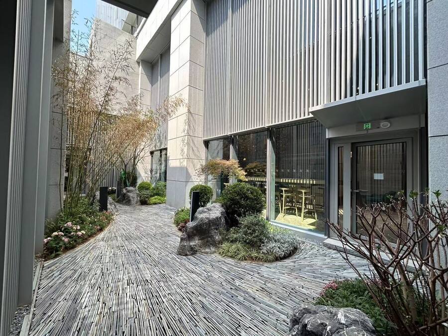 Un edificio moderno con un patio que presenta un paseo de madera, jardines rocosos y una entrada con puerta de vidrio.