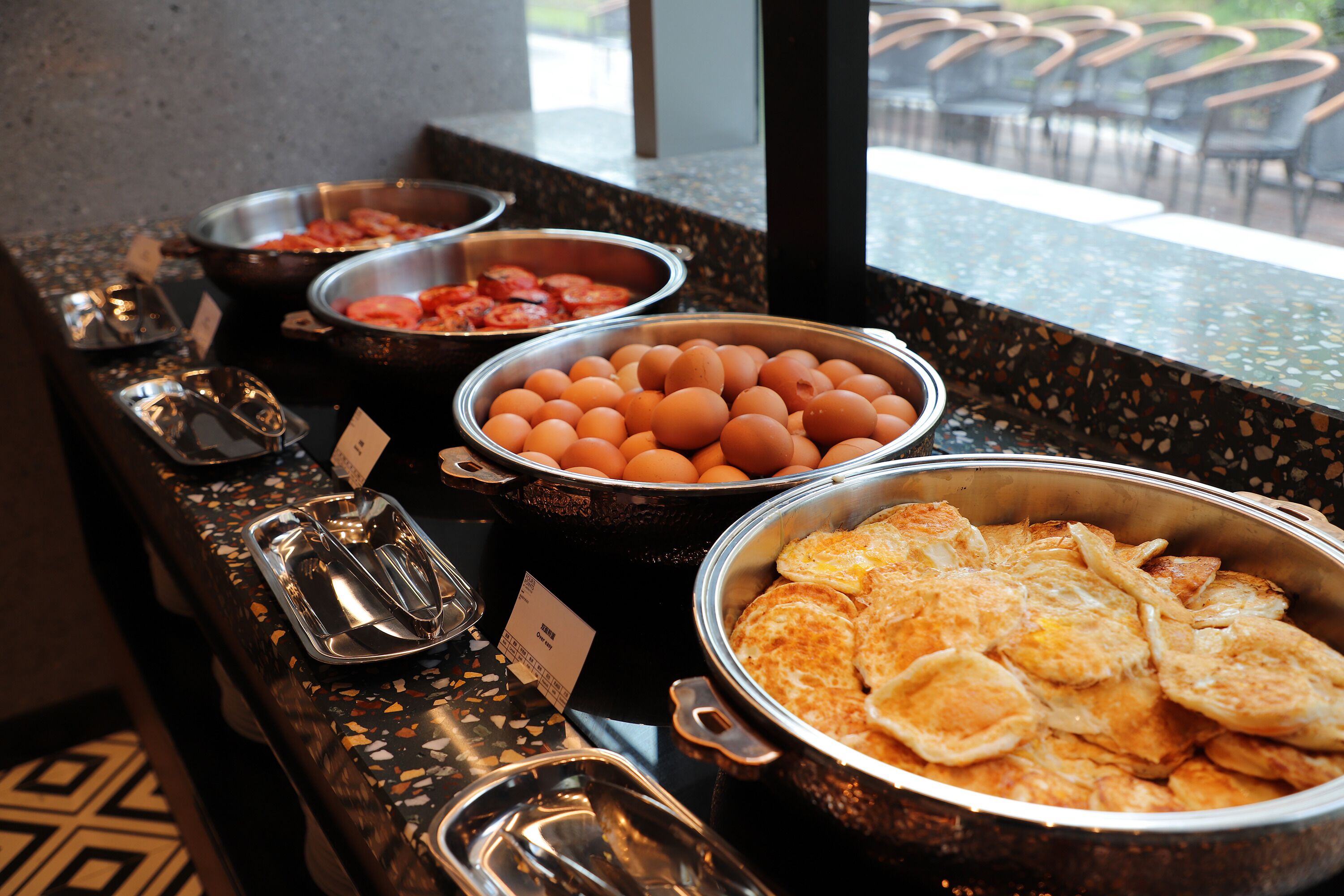 A buffet with various food items including eggs, tomatoes, and a large pot of scrambled eggs.