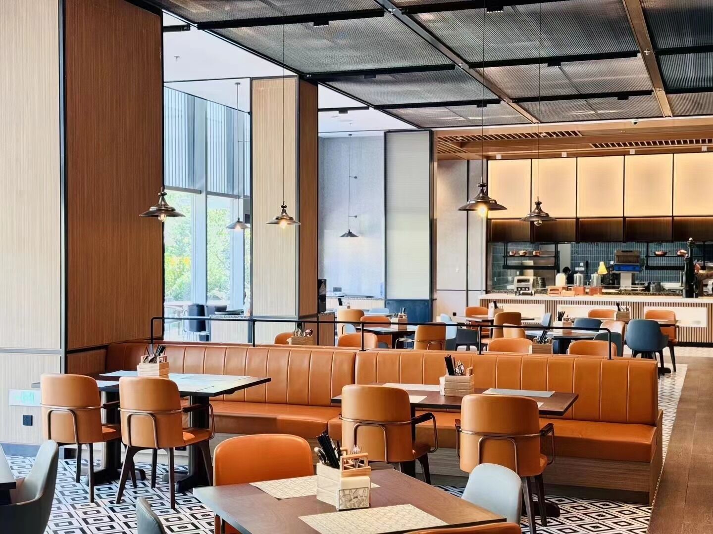 A modern restaurant with leather booths and tables, large windows, and a visible kitchen area.