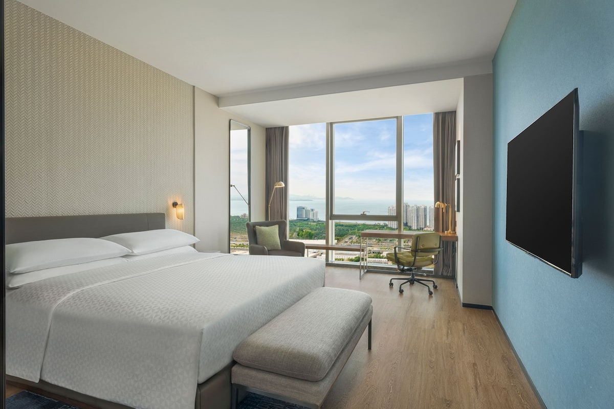 A modern hotel room with a large bed, a desk, and a TV.