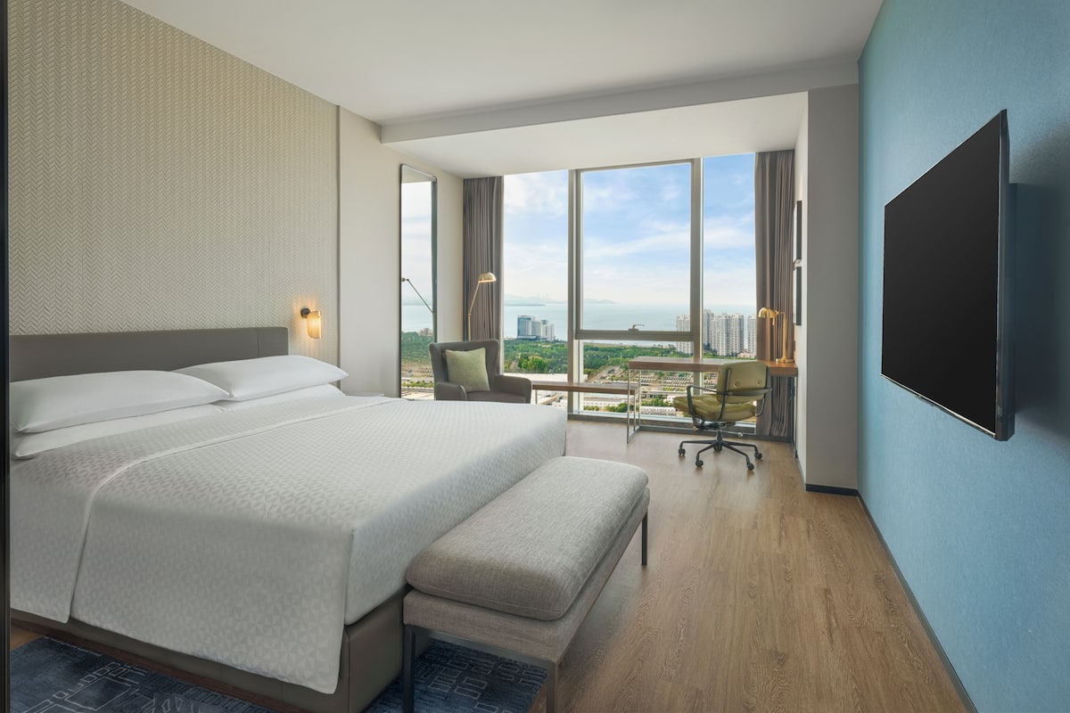 Moderni hotellihuone, jossa on suuri sänky, työpöytä ja näkymä kaupungin ylle.