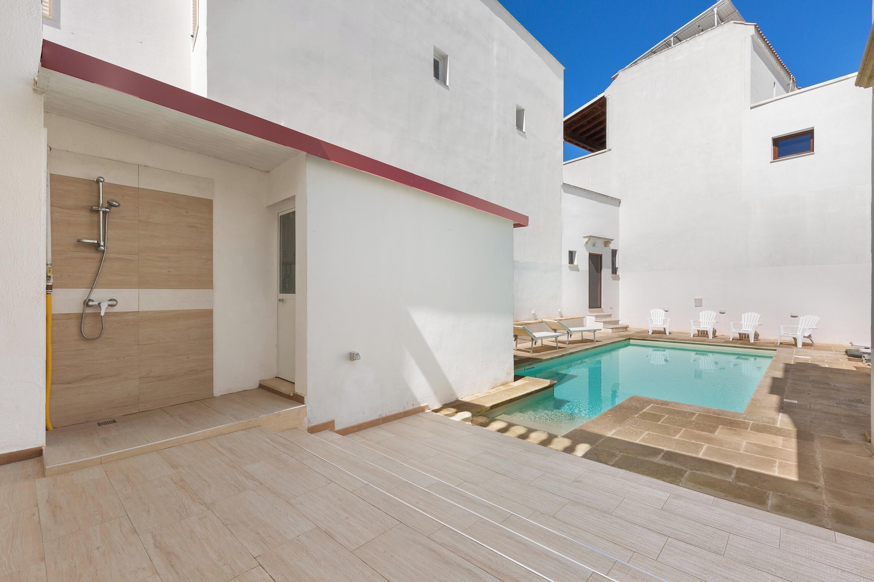 Un espace piscine extérieur moderne, doté d’une douche intégrée, de murs blancs et d’un sol carrelé.