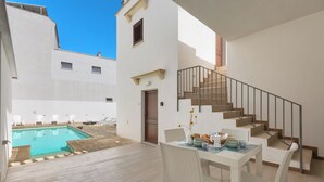Une terrasse extérieure moderne avec une piscine, des meubles en osier blancs et un escalier menant à l’étage supérieur.
