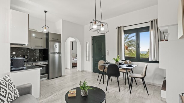 Un apartamento moderno con cocina, comedor y sala de estar. Cuenta con un refrigerador de acero inoxidable, una mesa de comedor con sillas, un sofá y un ventanal con vistas.